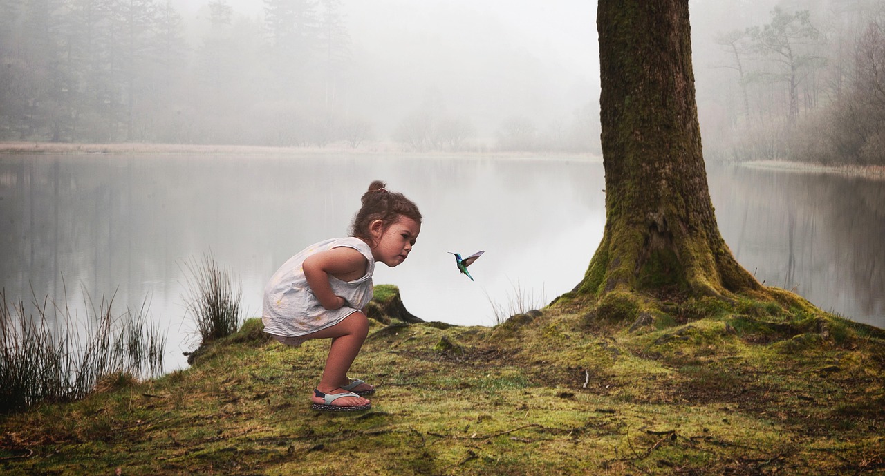 petite fille nez à nez avec un colibri au bord d'un lac
